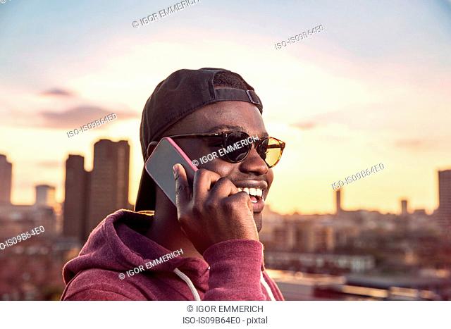 Young man making smartphone call at sunset roof party in London, UK