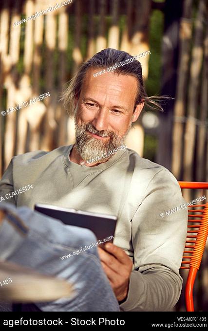 Close-up of bearded man reading book while relaxing on chair in yard