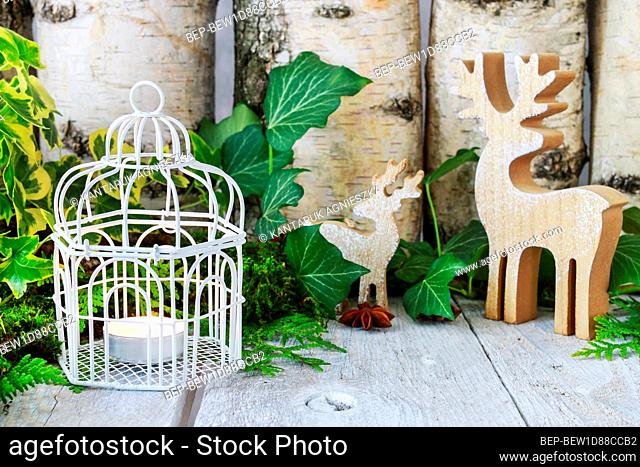 Two wooden deers and candle inside the vintage bird cage. Christmas table decoration in traditional style