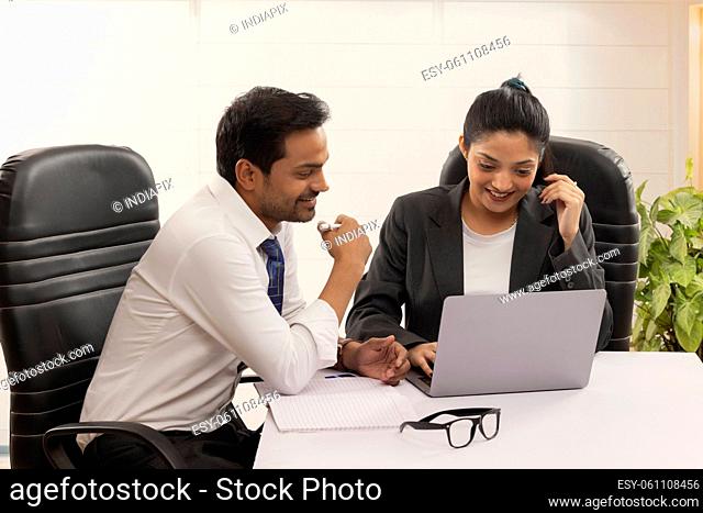 Happy business couple checking emails together using laptop in office