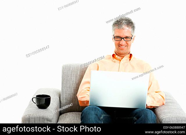 Mid-adult man wearing jeans and orange shirt sitting on couch, using laptop computer. Isolated on white