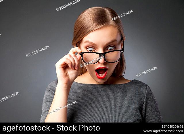 Amazed woman with red lips in glasses looking down with open mouth