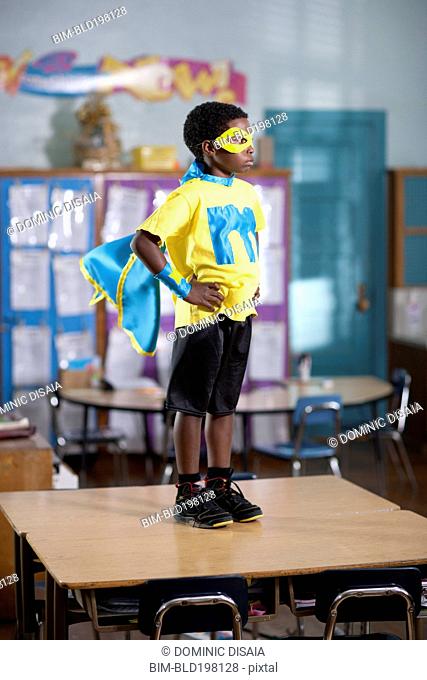 African American boy in superhero costume standing on desk