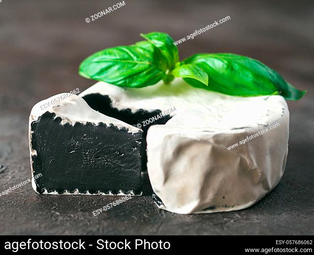 Unusual black camembert cheese with white mildew.Trendy modern cuisine, meal, food.Close up view of slice organic black camembert on black background