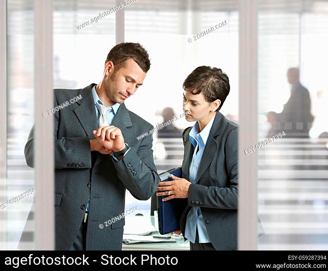 Businessman and businesswoman leaving meeting room, talking at the door, smiling