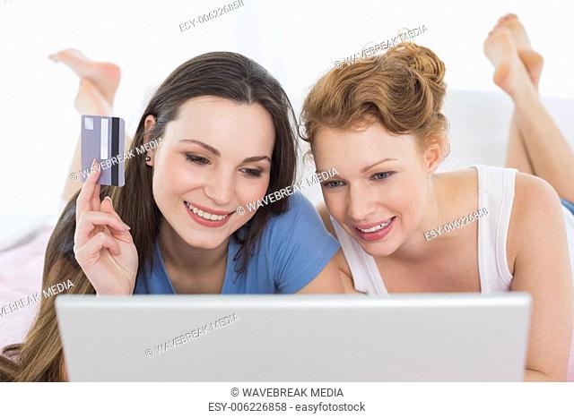 Relaxed female friends doing online shopping in bed