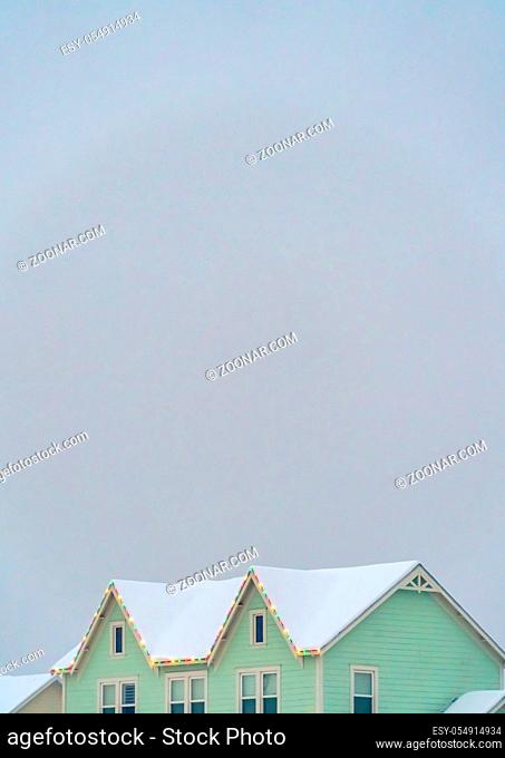 Snowy roof lined with colorful lights against sky. Snow covered roof of a home lined with bright colorful lights in December