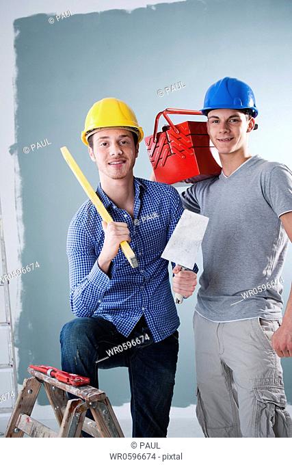 Two young men wearing hard hats holding tools
