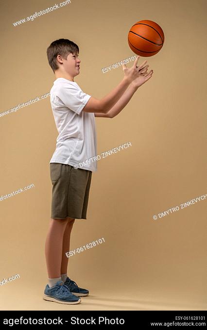 Side view of a concentrated adolescent throwing the game ball up against the beige background