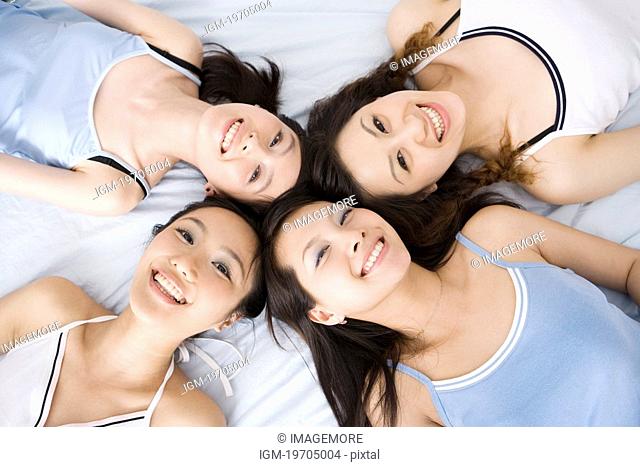 Four young women lying in circle on bed, overhead view