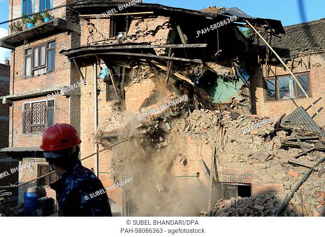 A Nepalese police officer watches the demolition work of a damaged house in Bungmati, Nepal, 05 May 2015. | usage worldwide. - Bungmati/Nepal