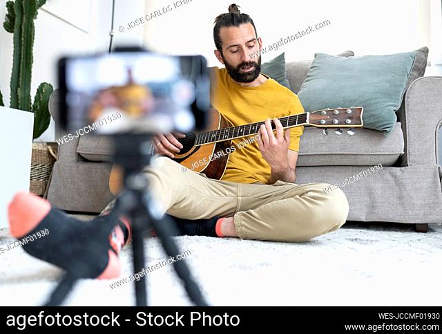 Male influencer vlogging while playing guitar at home
