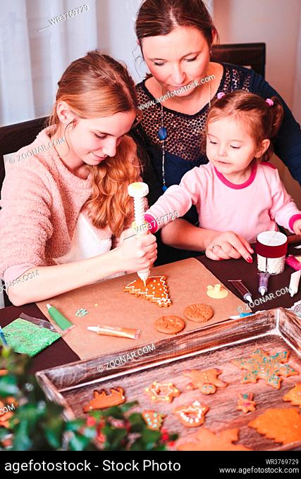 Family decorating baked Christmas gingerbread cookies with frosting
