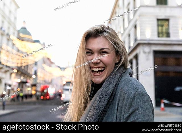 Young blond woman with blond hair laughing while standing in city