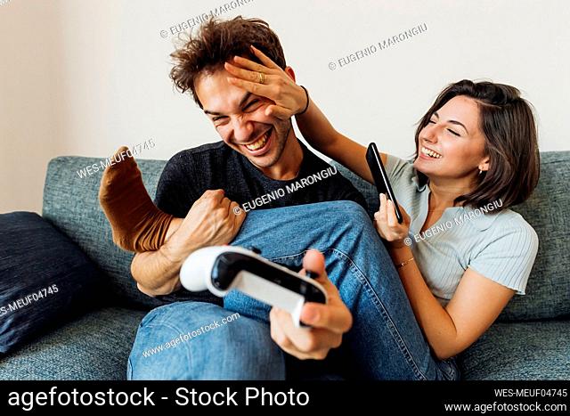 Playful young couple with game controller and smart phone at home
