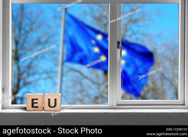 EU sign in a window with the European union flag outside waving in the wind