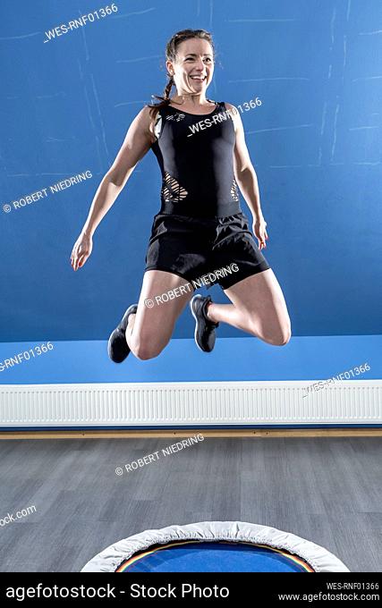 Smiling young woman jumping on small trampoline in fitness room