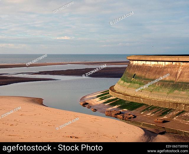 the concrete seawall of the old boating pool at blackpool lancashire surrounded by pools of water on the beach at low tide with a blue sea and clouds