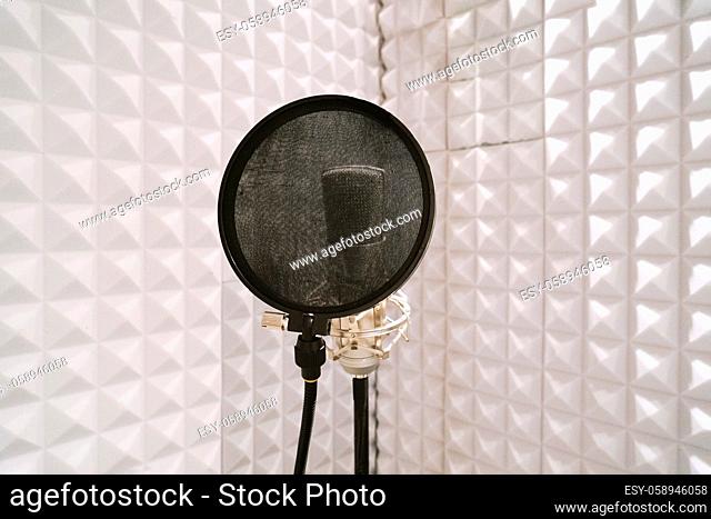 microphone with pop filter on mic stand in soundproof isolation booth for vocal recording at sound studio
