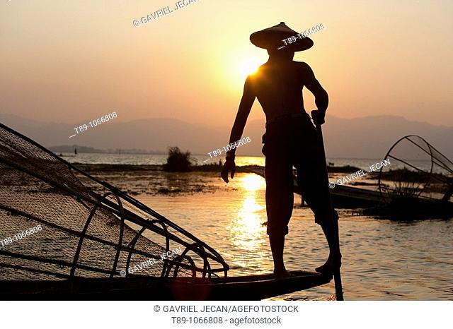 An Intha fisherman with traditional fish trap uses an unusual leg-rowing technique to propel his flat-bottomed boat across the lake while standing