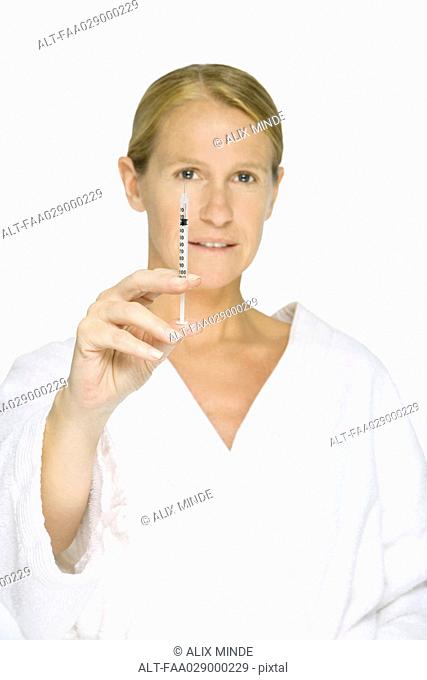 Woman in bathrobe holding up syringe, looking at camera