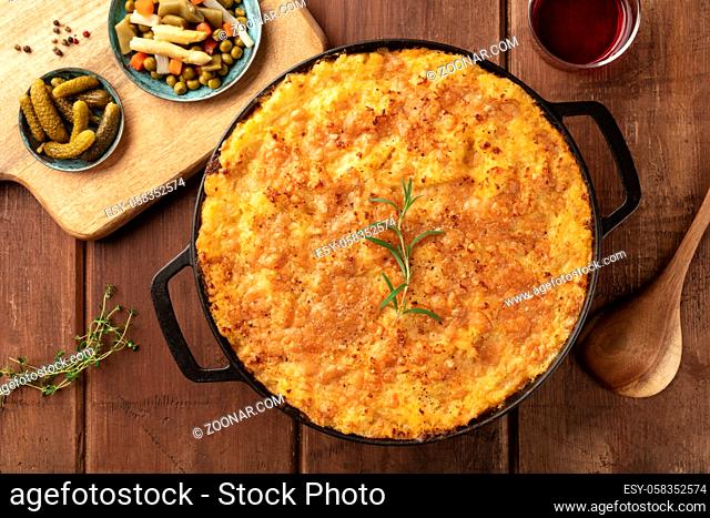 Homemade Shepherd's pie in a cooking pan with pickles, herbs, and wine, shot from the top on a dark rustic wooden background