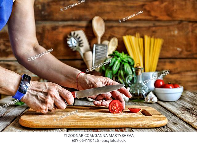 A woman cuts a cherry tomato and prepares a traditional Italian pasta. top veiw