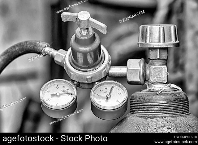 Brass reducer with two pressure gauges screwed on the cylinder with compressed gas. Black and white photo