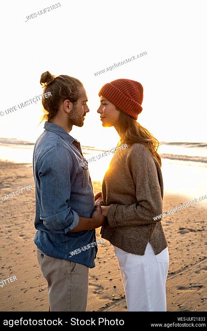 Romantic young couple looking at each other while standing on shore during sunset