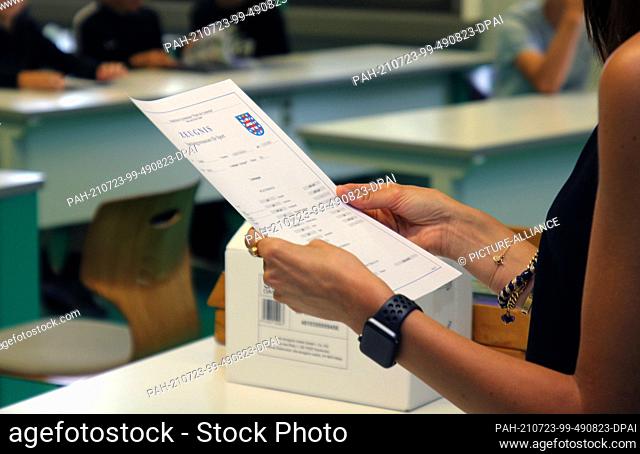 23 July 2021, Thuringia, Erfurt: A teacher at a high school stands in a classroom on the last day of school before summer vacation, report card in hand