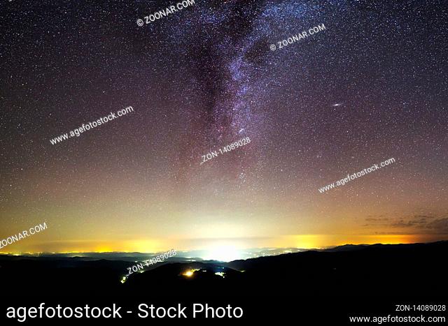 A view of a Meteor Shower and the Milky Way with an illuminated city silhouette in the foreground. Night sky nature summer landscape