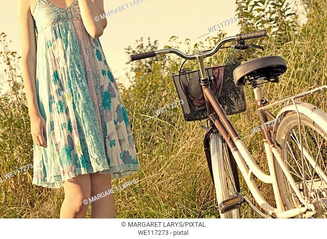 A young girl in a blue dress with a vintage bike in the meadow, waiting