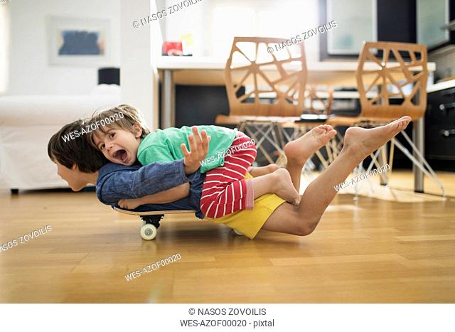 Two brothers at home lying on skateboard together having fun