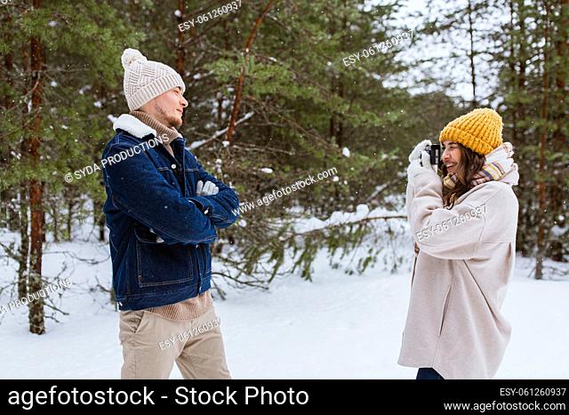 happy woman photographing man in winter forest