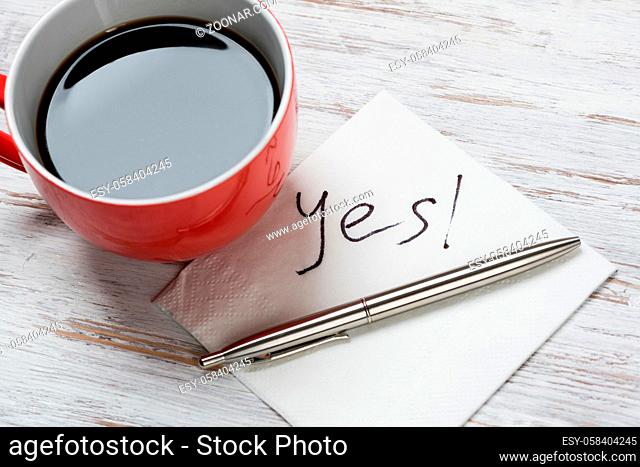 Cup of coffee and napkin with writings on table