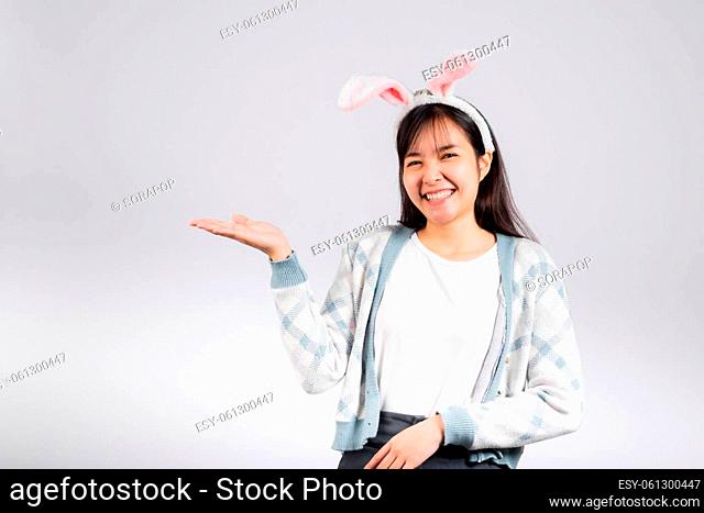 Easter day concept. Smiling happy woman wearing rabbit ears presenting product holding something on palm away side, studio shot isolated on white background...