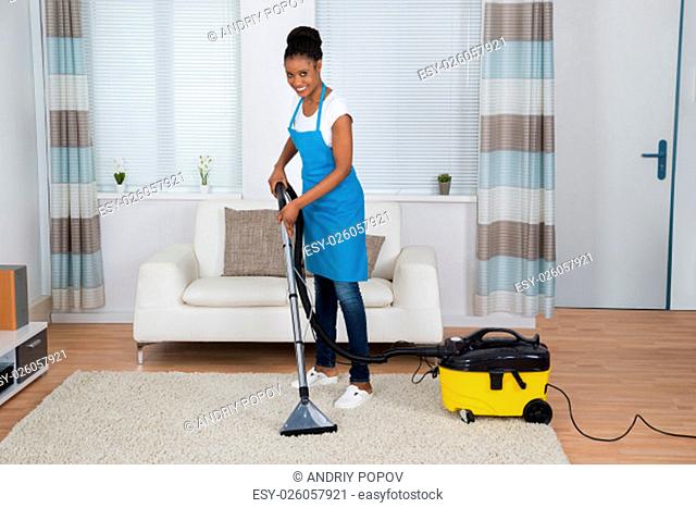 Smiling Young African Woman Cleaning Carpet With Vacuum Cleaner