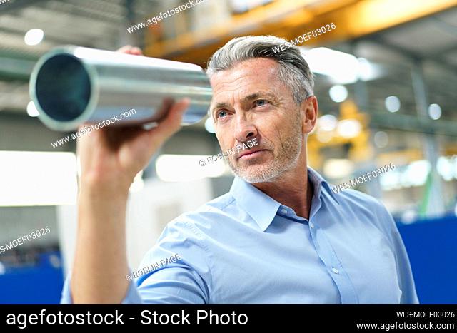 Businessman holding steel pipe in a factory