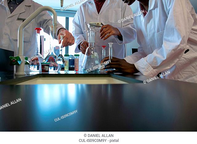 Male and female scientists preparing experiment with sample bottles in laboratory, mid section