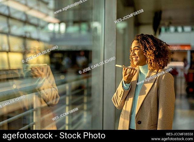 Happy woman talking through speaker mobile phone at station