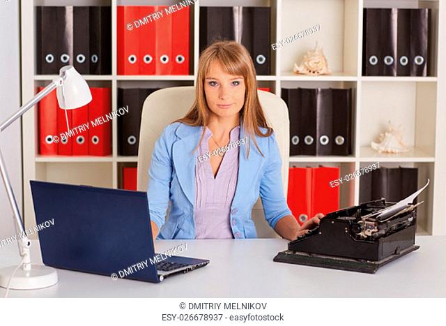 Young business woman with notebook and old typewriter sits on workplace in the office. Progressing of technology