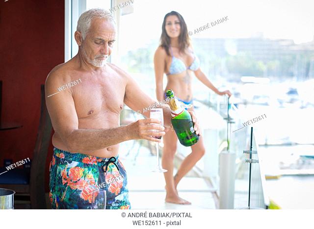 Older caucasian man pouring sparkling wine into glass for younger woman