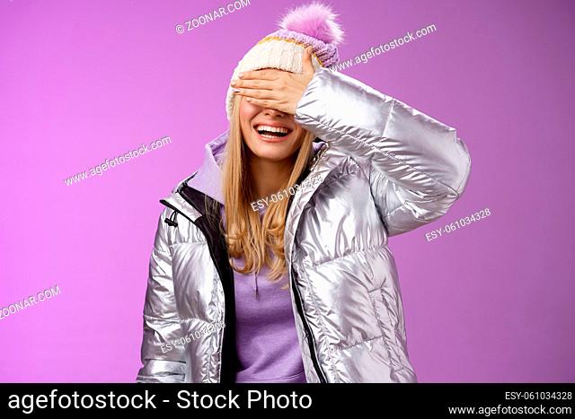 Happy relaxed smiling attractive young blond woman in stylish warm silver jacket hat hide eyes behind palm laughing happily waiting boyfriend prepared surprise...