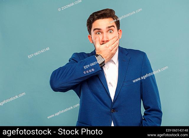 Surprised man with big eyes closed hands mouth . Business people concept, richly and success. Indoor, studio shot on light blue background