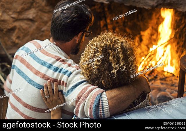 Romantic couple enjoy flame in front of fireplace in winter at home - cozy romance love man and woman viewed from back admiring fire to heat and enjoy...
