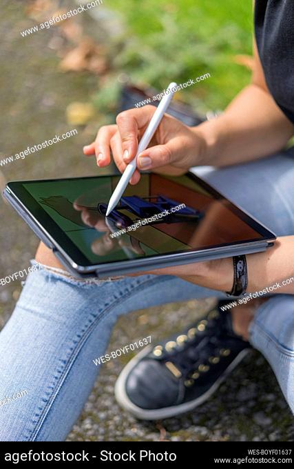 Hands of young woman drawing on digital tablet while sitting in park