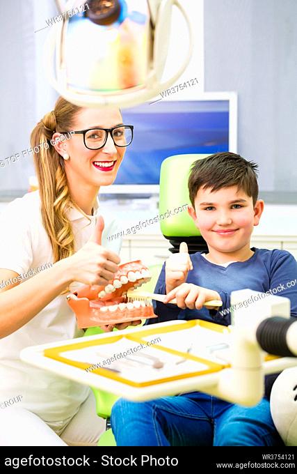 Female dentist explaining boy cleaning tooth with toothbrush on model