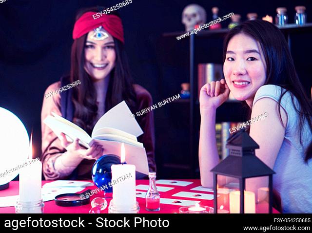 A beautiful Asian woman is performing a ritual for fortune telling with the fortune teller, a woman with a third eye and a sixth sense in a mysterious dark room