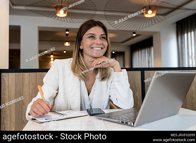 Happy businesswoman sitting with hand on chin at restaurant