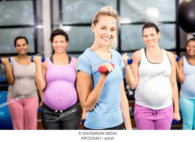 Female trainer with pregnant woman lifting dumbbells
